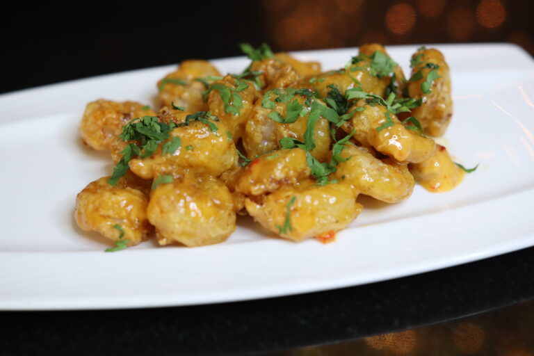 Golden, crispy prawns glazed with a shiny sauce are garnished with fresh cilantro on a white plate. The setting is elegant and appetizing.