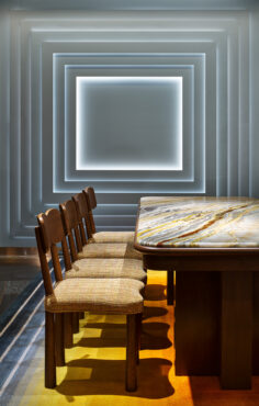 Geometric dining room with glowing square wall lights, a marble table, and four wooden chairs on a colorful gradient rug, creating a modern, warm tone.