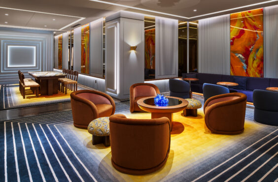 Modern lounge with circular orange chairs around a glass table featuring blue decor. Bright abstract art and sleek lighting create a cozy, elegant ambiance.