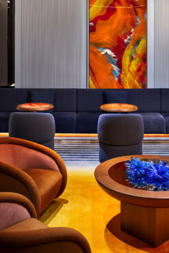 Modern lounge with orange and brown chairs on a yellow carpet. Abstract red and yellow painting on the wall. Round table with blue decorative piece. Cozy ambiance.