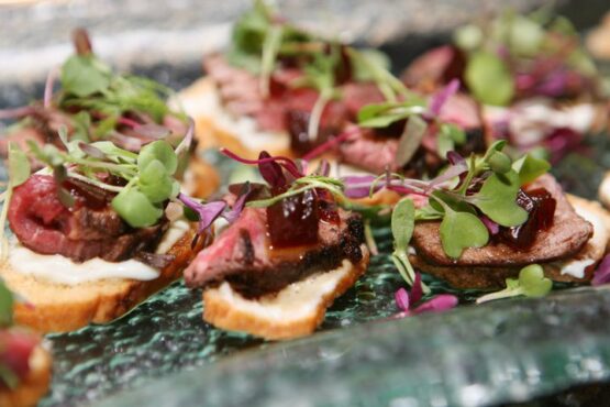 A glass plate elegantly arranged with tenderloin crostinis, showcasing exquisite small appetizers for a refined gathering.